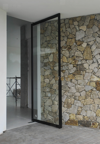 Large frameless glass pivot door installed against a natural stone feature wall.