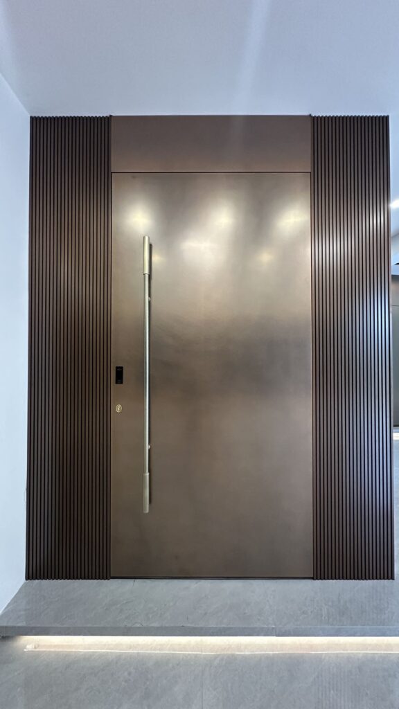 Engineering Excellence in Residential Pivot Door Installation: A Technical Case Study Sleek minimalist bronze pivot door with a long vertical handle and matching fluted wall panels.
